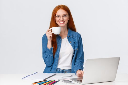 Cheerful and energized good-looking redhead female freelancer, drink too much coffee smiling excited and thrilled, working over creative cool project, using laptop, drawing, white background.