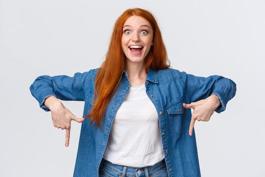 Waist-up portrait happy, lucky redhead girl winning prize, achieve goal in challenge, celebrating, showing people product, looking amused with pretty smile, pointing fingers down, white background.