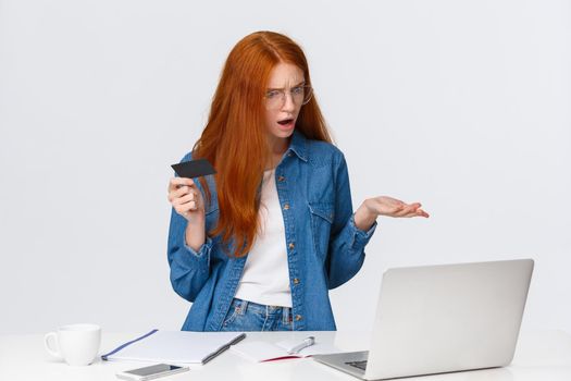 Perplexed and confused redhead woman cant make online purchase, dont know why problem with transferring money occused, shrugging pointing in dismay at laptop screen, hold credit card, complain.