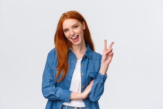 Business, university and people concept. Attractive cheerful redhead woman in denim shirt, send positivity and happiness, showing peace sign and smiling carefree, standing white background.