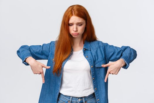 Upset, gloomy timid redhead teenage girl express pity or jealousy, regret something broken, sobbing, pouting sad and looking pointing down distressed, standing unhappy over white background.