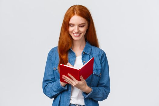 Creative and talented good-looking female college student prepare schedule for tomorrow classes, writing in diary, taking notes in fancy notebook, standing white background.