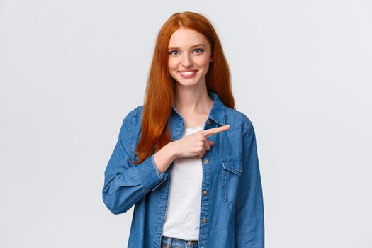 Waist-up portrait friendly smiling, happy redhead confident female student in denim shirt, showing where good courses online, pointing finger right and grinning, invite join, white background.