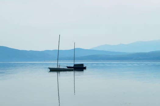 boat with masts on the water surface against the background of mountains in blue tones.