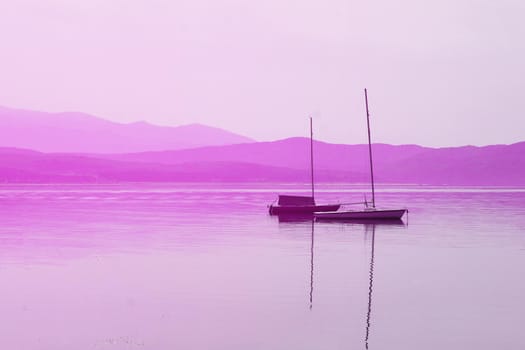 boat with masts on the water surface against the background of mountains in pink tones.