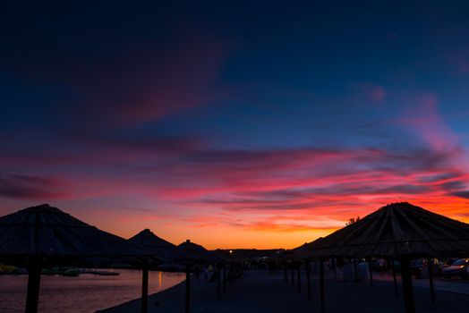 Beach umbrellas, view of the beautiful blue and purple sunset, sky and straw beach umbrellas. Perfect holiday concept. Travel and vacation. Beach on Vir Island, Croatia, Europa. Copy space.