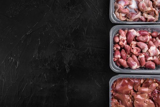 Raw uncooked Bird chicken giblets gizzards, stomachs, liver, offal, hearts set, on black dark stone table background, top view flat lay, with copy space for text
