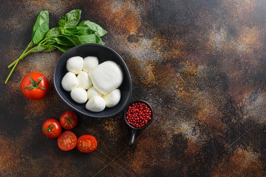Tasty mozzarella cheese with basil and tomatoes in black bowl, ingredients for salad Caprese. on old rustic metal background. Caprese salad ingredients. Selective focus. top view space for text