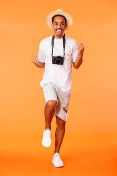 Full-length vertical shot excited good-looking african american guy on joyrney abroad, travelling feeling amused, fist pump, winning trip travel agency, dancing, standing orange background.