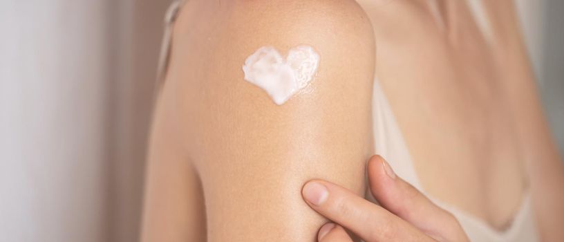 A young girl applies a moisturizer to her skin, a woman gently cares for her body, depicts a heart with a cream, taking care of herself, beauty and health.