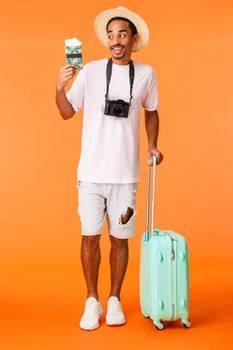 Full-length vertical shot excited happy african-american male traveller, cant wait sip cocktail under sun and enjoying awesome vacation, holding luggage, suitcase and passport with tickets.