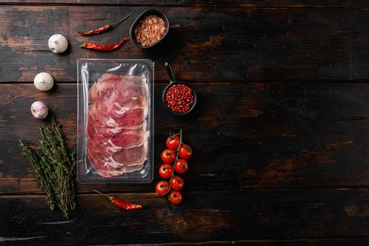 Vacuum packed serrano ham set, on old dark wooden table background, top view flat lay, with copy space for text