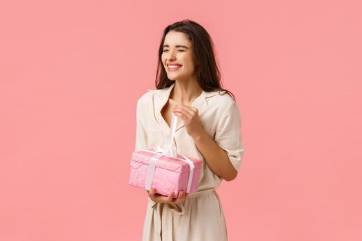 Happiness, celebration and anniversery concept. Happy and carefree cheerful b-day girl unwrapping cute present smiling and laughing with closed eyes, feeling joyful, open gift for birthday.