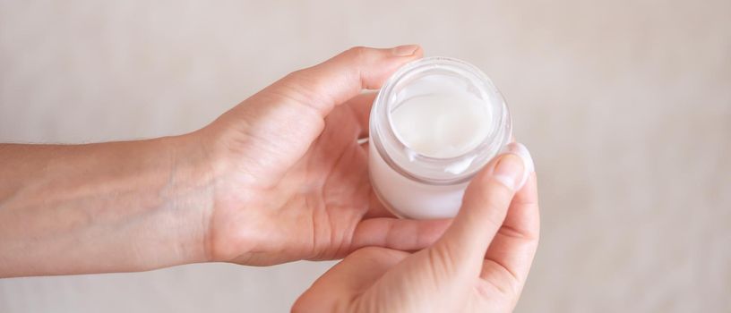 Young female hands hold a jar of moisturizing cream to maintain health, softness of the skin, the woman takes care of her health and beauty.