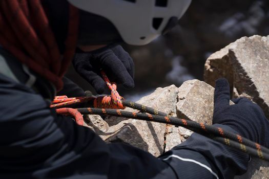 A young man in a helmet and with climbing equipment descends from the top of the mountain on a rope, the climber rappels with aperture-style self-braking belay in the snowy mountains.