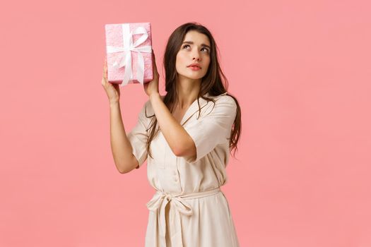 Celebration, women and anticipation concept. Alluring curious young woman shaking gift box with interest, focus, intrigued what inside, standing pink background, receive present.