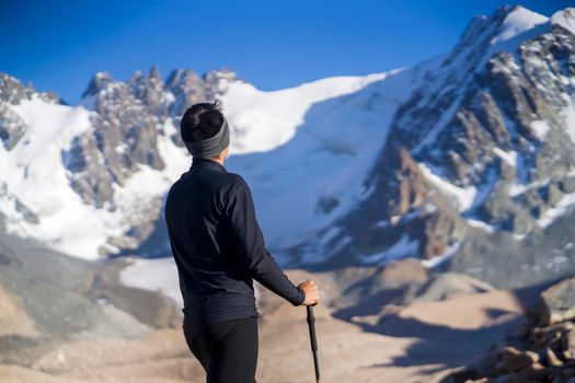 A young man travels, goes to the mountains in thermal underwear and with trekking poles, a hiker climbs to the top of the mountain, against the backdrop of red rocks and a glacier.