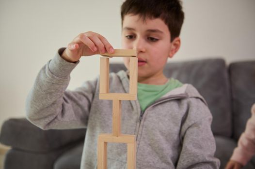 Close-up of the hand of European handsome puzzled schoolboy, concentrated on construction of complex tall structure from wooden blocks. Fine motor skills, concentration and educational leisure concept