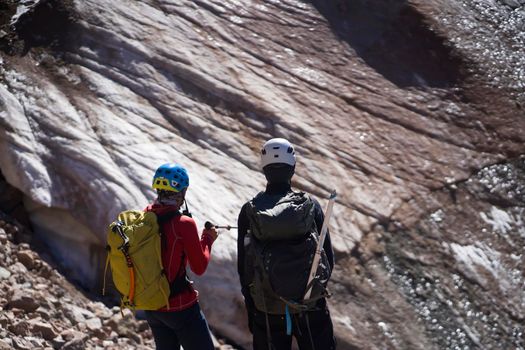 Two climbers discuss, plan a route to the summit and climb a glacier in the mountains with tourist equipment, people in helmets, with a rope and backpacks travel on rocky terrain.