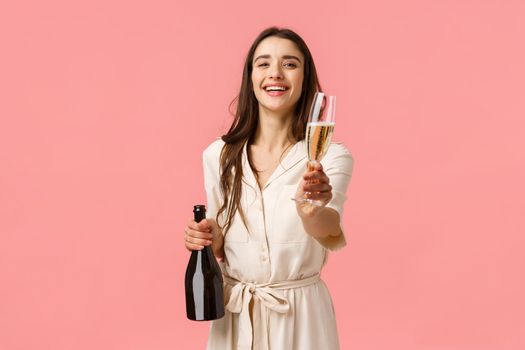 Here drink. Romantic tender young brunette woman opened bottle champagne laughing and smiling giving glass to girlfriend, suggest celebrate special occasion together, pink background.