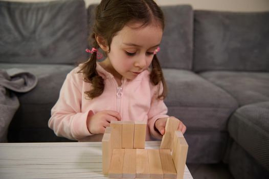 Adorable Caucasian 4 years old baby girl building house with wooden bricks and blocks. Hand movement control and concentration skills concept, educational board games