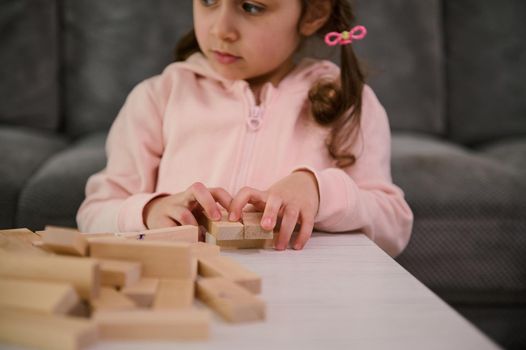 Soft focus on the hands of a cute baby girl, on wooden blocks, while she playing developmental and educational board game, building structures from bricks. Fine motor skills development concept