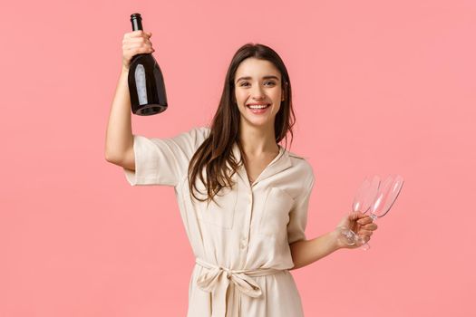 Raise your glasses ladies. Carefree happy young woman celebrating bachelorette party, holding champagne bottle and glass, smiling say cheers, having fun, partying over pink background.