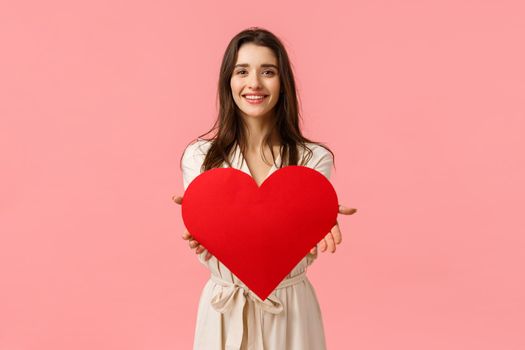 Here my love to you. Charming tender and alluring, romantic young woman giving big heart card to camera, smiling delighted, express her affection and admiration, standing pink background.