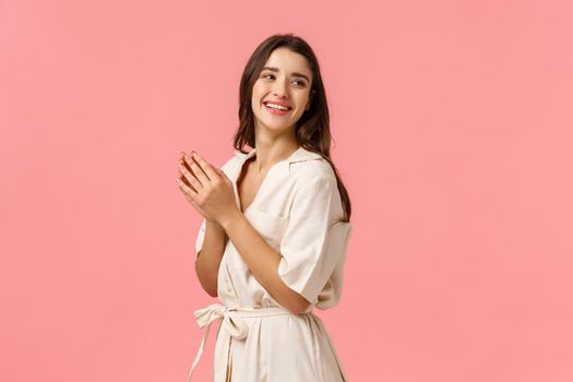 Fashion, leisure and beauty concept. Cheerful elegant and tender female tourist relaxing on spa resort, applying body lotion, hand cream, looking behind right side copy space, pink background.