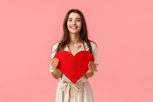 Spread news love in air. Charming sweet and tender feminine girl want surprise girlfriend with valentines day surprise date, holding heart card and smiling, standing pink background.