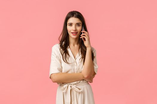 Waist-up portrait serious and gorgeous sassy young woman in dress, holding smartphone, talking on phone, calling friend, having conversation, checking with order, standing pink background.