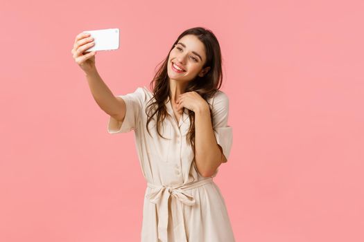 Tenderness, beauty and fashion concept. Lovely young alluring woman posting photo online, video-calling friend, holding smartphone raised as taking selfie, tilt head making cute expression.