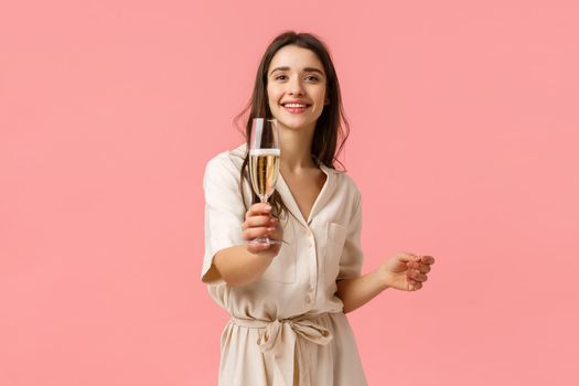 Here, make a toast. Cheerful romantic and alluring young girlfriend extending hand with glass, giving champagne to boyfriend, smiling joyfully, enjoying awesome party, pink background.