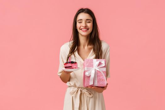 Cheer, happiness and celebration concept. Happy carefree funny young gorgeous woman close eyes dreamy and smiling, receiving congratulations, hold cake and gifts, pink background.