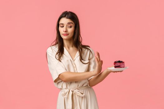 No thank you. Girl having strong will, reject piece cake, holding plate and making stop, refusal motion with determined, assertive expression, standing pink background, stick to diet.