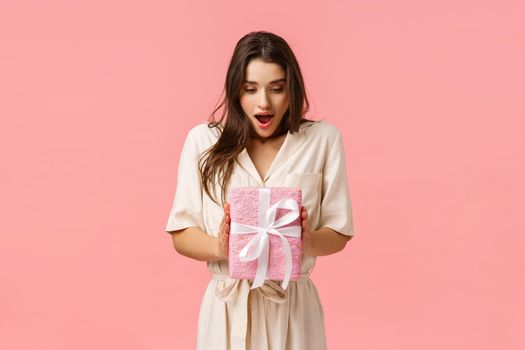 Amazement, celebration and holidays concept. Surprised girlfriend holding box of present, didnt expact receive gift, open mouth fascinated look touched wrapped box, pink background.