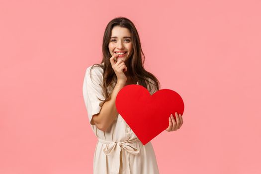 Romance, beauty and happiness concept. Sensual alluring, coquettish young woman in dress, touching lip express desire or temptation, smiling want try something, holding red big heart, valentines day.