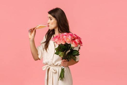 Girl sipping champagne from glass as peeking at someone, wearing elegant dress, celebrating, having party, receive roses, bouquet flowers, standing pink background intrigued and amused.