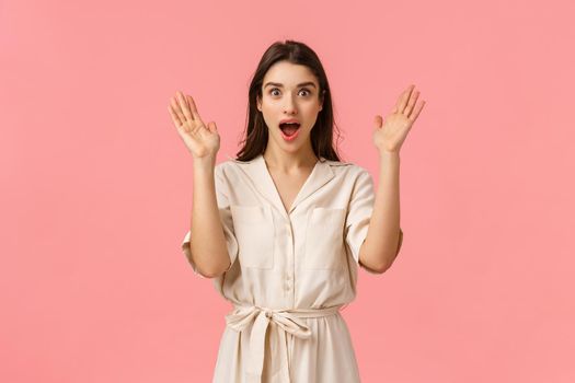 Wow super surprise. Amazed and wondered, excited happy, glad pretty caucasian woman in cute dress, raise hands up astonished, open mouth and looking camera thrilled, standing pink background.