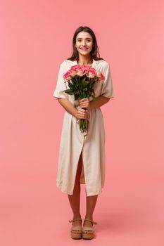 Full-length vertical portrait attractive, lovely young woman receiving beautiful flowers, holding bouquet enjoying romantic date, smiling happily, standing pink background delighted.