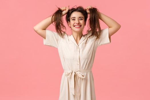 Joy, party and happiness concept. Silly funny girl having fun fooling around, pulling hair sideways making it messy, smiling cheerfull, enjoy perfect day feeling amused and upbeat, pink background.