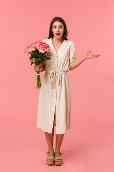Full-length vertical portrait surprised see boyfriend with flowers, receive charming bouquet, spread hand sideways and shrugging surprised, look wondered and astonished, standing pink background.