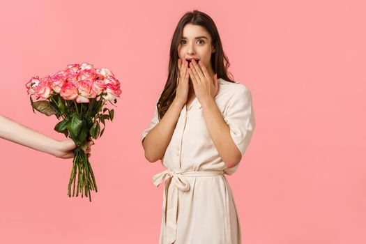 Surprises, gifts and romantic gestures concept. Charming amused cute caucasian brunette female looking amazed and wondered as reacting on boyfriend giving her roses, big lovely flowers bouquet.