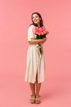 Full-length vertical portrait romantic ecstatic young woman receiving touching gift, embracing cute bouquet roses, looking dreamy and delighted, smiling thoughtful, pink background.