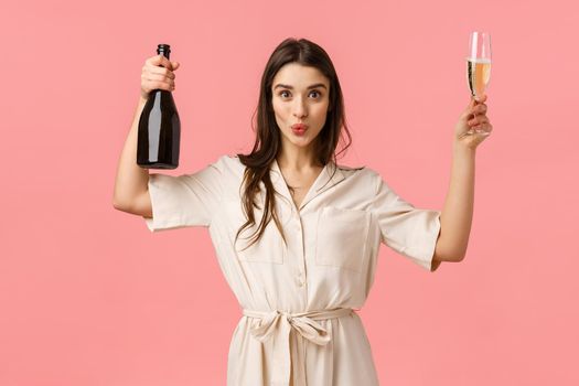 Women, celebration and party concept. Fashionable good-looking brunette female in dress, having fun, praying, open champagne bottle, raising glass suggesting drink and celebrate.
