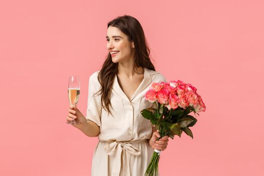 Elegance, celebration and party concept. Attractive young happy woman having birthday, receiving gifts, beautiful flowers, holding roses and champagne glass, smiling left, pink background.