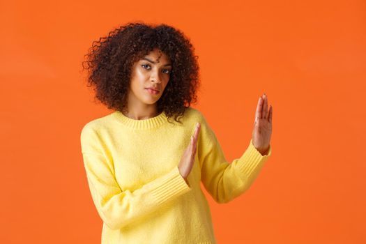 I said no. Serious-looking assertive and determined african-american woman looking camera and make stop, refusal gesture to right side, decline offer, feel reluctant, standing orange background.