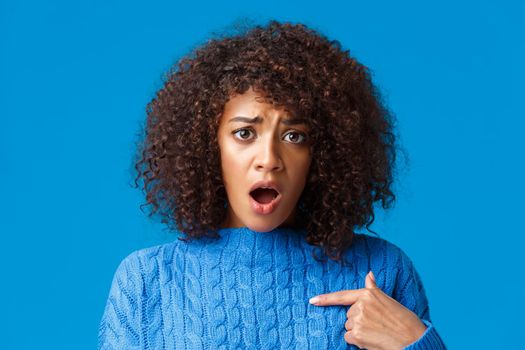 Close-up portrait offended and upset silly timid african-american woman was accused or blamed, pointing herself and looking insulted, gasping staring at something unfair, standing blue background.