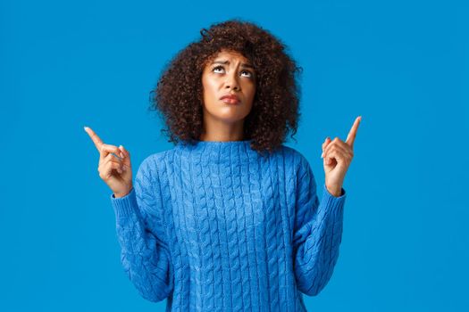 Skeptical and upset, gloomy timid african-american woman dont like whats happening, express disapproval and sadness, looking pointing up jealous, envy of friend bought she wanted, blue background.