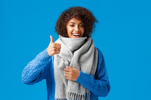 Very good, yes. Cute happy african-american woman in sweater, bought cool warm and comfortable scarf showing thumb-up in approval, recommend shop, standing blue background.